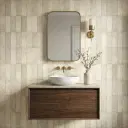 Modern bathroom vanity with wooden cabinet, round white basin, oval mirror, and beige vertical patterned wall tiles in a soft textured finish